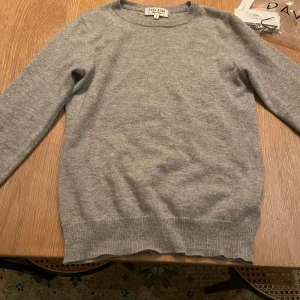 Grå kashmirtröja från Davida - Säljer en mjuk och stilren grå kashmirtröja från Davida. Tröjan har en klassisk design med rund hals och långa ärmar, perfekt för kyligare dagar. Ett måste i garderoben för den som älskar komfort och stil.