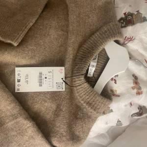 Beige stickad tröja från Uniqlo - Säljer en mysig beige/brun stickad tröja från Zara. Tröjan har en croppad passform med långa ärmar och ribbade muddar vid ärmslut och nederkant. köpt förra julen men aldrig använd! kan gå ner i pris😇