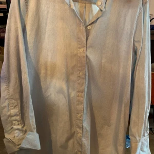 Ljusblå skjorta från By Malene Birger - Elegant ljusblå skjorta från By Malene Birger med diskret mönster. Skjortan har långa ärmar och knappar framtill. Perfekt för en stilren look.