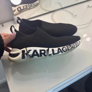 Svarta sneakers från Karl Lagerfeld - Stilrena svarta sneakers från Karl Lagerfeld med elastisk passform och vit sula. Skorna har märkets logotyp i svart och vitt längs sulan och är perfekta för en modern look.