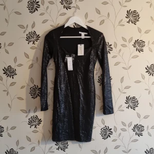 Svart paljettklänning från NLY Trend, Strl: 36/S - Snygg svart klänning från NLY Trend med glittrande paljetter. Den har en figurnära passform och långa ärmar, perfekt för festliga tillfällen. Klänningen har en dragkedja i ryggen för enkel påklädning. Nyskick! Lapparna kvar. Se bilder.