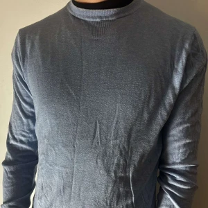 Blå tröja från Tommy Hilfiger - Säljer en stilren blå tröja från Tommy Hilfiger i mjuk Pima bomull. Tröjan har en klassisk design med långa ärmar och rund hals. Perfekt för en avslappnad men ändå elegant look.