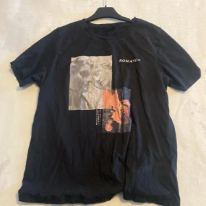 Svart t-shirt med tryck från Gina Tricot - Snygg svart t-shirt från Gina Tricot med ett konstnärligt tryck och texten 'ROMANCE' på framsidan. Perfekt för en avslappnad stil med en touch av konst. Det står XL men den är nästan lika stor som en M-L. 