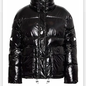 Svart glansig pufferjacka - Snygg svart pufferjacka med glansig finish. Jackan har en hög krage och dragkedja framtill. Helt oanvänd med prislapp kvar även kvitto om man vill ha de, pris kan diskuteras