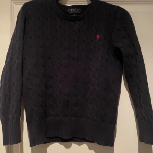Mörkblå stickad tröja från Ralph Lauren - Säljer en stilren mörkblå stickad tröja från Ralph Lauren med det klassiska logotypbroderiet i rött på bröstet. Tröjan har en rund halsringning och långa ärmar, perfekt för kyligare dagar. Storleken är i M fast för barn. Passar för runt 10-12 åringar.