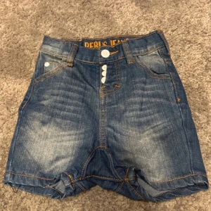 Blå jeansshorts från Peris Jeans - Snygga blå jeansshorts från Peris Jeans med hög midja och tre knappar framtill. Klassisk femficksdesign och slitna detaljer för en trendig look. Perfekta för sommardagar!