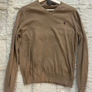 Beige tröja från Ralph Lauren - Säljer en snygg beige tröja från Ralph Lauren i Pima bomull i mycket bra skick. Den har en klassisk v-ringning och långa ärmar. Perfekt för både höst och vår. Tröjan är i mycket bra skick och har den ikoniska loggan broderad på bröstet.