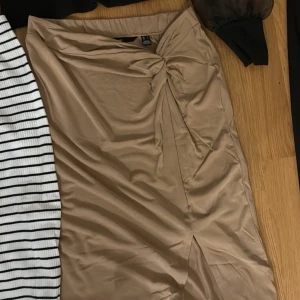 Beige omlottkjol - Säljer en superfin beige omlottkjol i sidenliknande material. Den har en elegant knytdetalj i midjan och en liten slits framtill som ger en chic touch. Perfekt för både fest och vardag! 🥰