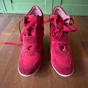 Röda sneakers med kilklack - Snygga röda sneakers i mocka med kilklack och snörning. Storleken är 40 men passar bra på mig som har storlek 37-38. De har en cool design med randigt foder och en vit sula.