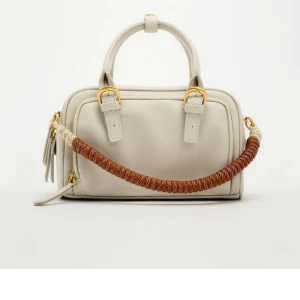 NYTT Vit handväska, zara - Helt nytt, aldrig använt! Snygg vit handväska i skinn med en unik flätad axelrem i brunt och beige. Väskan har guldfärgade detaljer och en praktisk dragkedja. Perfekt för både vardag och fest!