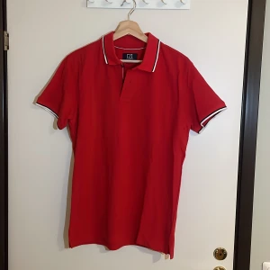 Röd pikétröja från Cutter & Buck - Säljer en snygg röd pikétröja från Cutter & Buck i storlek M. Tröjan har korta ärmar och en klassisk krage med vita och svarta detaljer. Perfekt för både vardag och festliga tillfällen. Priset kan alltid förhandlas!