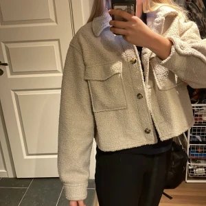Beige teddyjacka från H&M - Säljer en supermysig beige teddyjacka från H&M i storlek M men känns mer som en S. Jackan har en croppad stil med knappar framtill och två stora fickor på bröstet. Perfekt för hösten och våren. 🧥✨