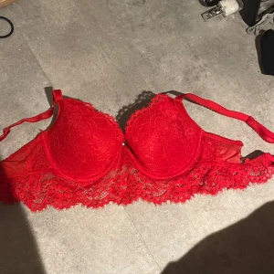 Röd spets-bh - Säljer en röd bh med vacker spetsdetalj. Den har ett hål vid sidan, nedre bandet men inget som syns eller känns, storlek S, ingen aning vilken kupa men kom privat för o se hand bredvid typ eller hur den sitter på