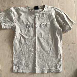 Beige t-shirt från Nicce - Säljer en snygg beige t-shirt från Nicce i storlek XS. Den är i bomull och har korta ärmar. Perfekt för en avslappnad stil. Texten 'NICCE' är tryckt på framsidan. Passar bra till både vardag och fest!