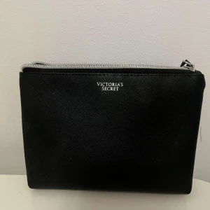 Svart necessär från Victoria's Secret - Säljer en superfin necessär från Victoria's Secret i svart  Perfekt för att förvara smink eller andra småsaker. Den har en praktisk dragkedja upptill. Perfekt för resor eller att ha i väskan till vardags!
