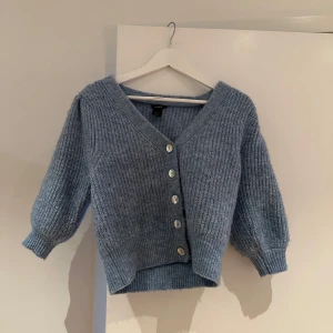 Blå ribbad kofta - Mysig blå kofta med ribbad struktur och knappar framtill. Den har en v-ringad design och trekvartsärmar, perfekt för lager på lager under höst och vår. Koftan är i mycket bra skick och ger en avslappnad men stilren look.
