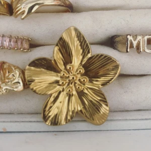 Guldfärgad blomring - Snygg och iögonfallande guldfärgad ring formad som en blomma. Perfekt för att ge en touch av glamour till vilken outfit som helst. Blomman har detaljerade kronblad och en glansig finish som verkligen fångar ljuset. Passar både till vardag och fest!