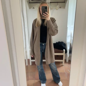 Beige lång kofta - Mysig och oversized beige kofta i ull. Perfekt för höst och vinter med långa ärmar och en avslappnad passform. Den är superbekväm och passar till alla tillfällen. 