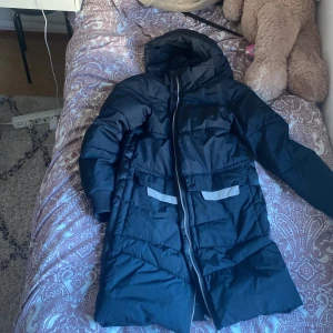 Svart dunjacka från Everest - Säljer en svart dunjacka från Everest i mycket bra skick. Den är lång och perfekt för kalla vinterdagar. Jackan har en luva  och stängs med dragkedja. Den har också praktiska fickor med lock. Supermysig och varm, perfekt för vintern! andvänd en gång.❄️