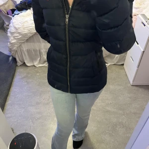 Mörkblå dunjacka från Tommy Hilfiger - Säljer en snygg mörkblå dunjacka från Tommy Hilfiger. Jackan har en dragkedja framtill och en mysig huva med fuskpäls. Perfekt för kalla vinterdagar! Den är i mycket bra skick och passar perfekt till både vardag och fest. Storlek dam M.