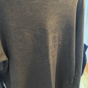 Säljer en stilren grå sweatshirt från Boss i mycket bra skick. Tröjan har en diskret broderad logga på framsidan och är gjord i mjukt bomullsmaterial. Perfekt för både vardag och avslappnade tillfällen. Passar till allt!