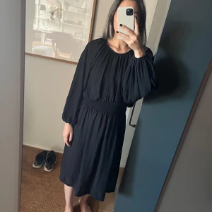 Weekday svart klänning, storlek XS - Svart klänning med långa ärmar och elastisk midja. Klänningen har en lös passform och är perfekt för både vardag och fest.