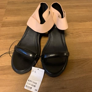 Svart och beige sandaler från H&M - Snygga sandaler från H&M i svart och beige. De har en bekväm klack och en stilren design med en bred rem över foten och en justerbar rem runt ankeln. Perfekta för sommarens alla tillfällen! 🖤