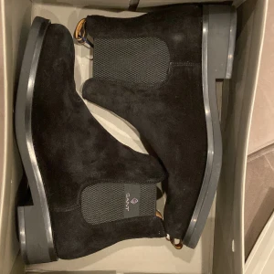Svarta Chelsea boots från GANT - Snygga svarta Chelsea boots i mocka från GANT. De har en klassisk design med elastiska paneler på sidorna för enkel på- och avtagning. Perfekta för både höst och vinter, och de ger en stilren touch till vilken outfit som helst. Skorna är i mycket bra skick dem är helt nya.