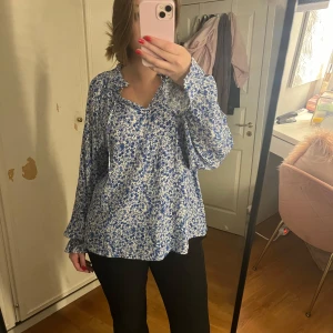 blommigblus - Jättefin blus i ett blå/vitt blommigt mönster, och en fin vringning. Perfekt till jeans eller kostymbyxor!