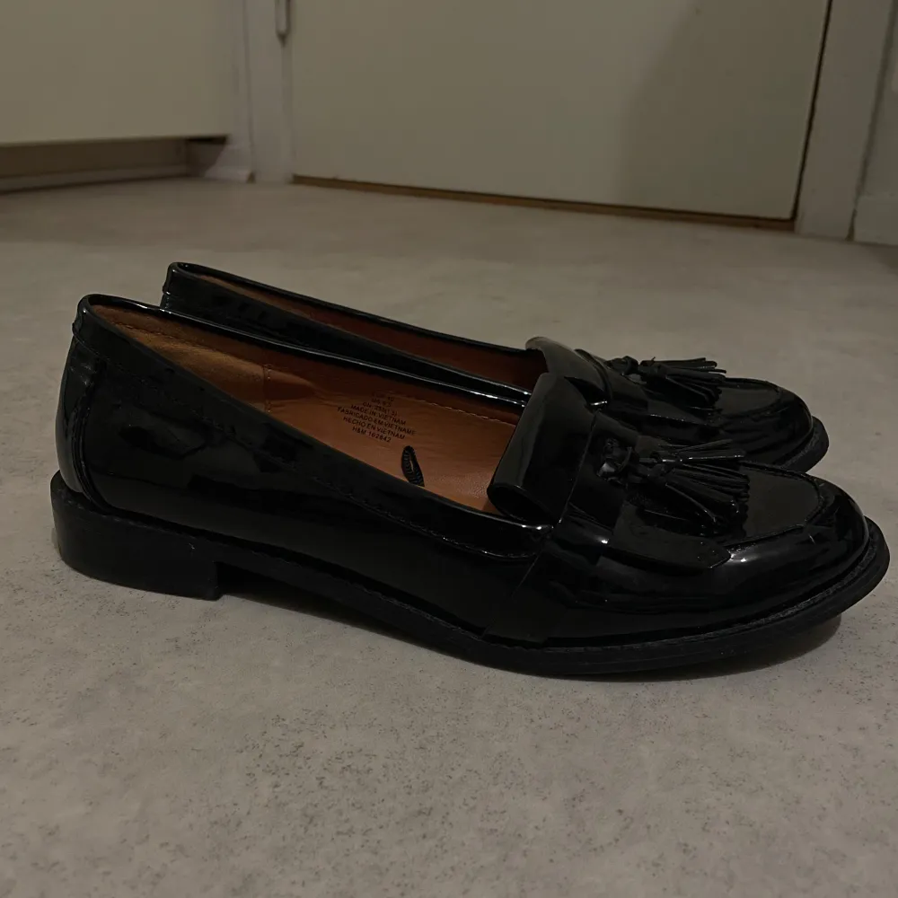 Snygga svarta loafers i skinn med dekorativa tofsar på ovansidan. Perfekta för både vardag och festliga tillfällen. De har en klassisk design med låg klack och en bekväm passform.. Skor.