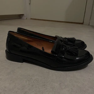 Svarta loafers med tofsar - Snygga svarta loafers i skinn med dekorativa tofsar på ovansidan. Perfekta för både vardag och festliga tillfällen. De har en klassisk design med låg klack och en bekväm passform.