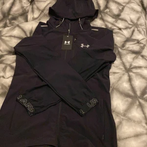 Svart jacka från Under Armour - (Säljer pågrund av att min son inte ville ha den modellen)Säljer en svart jacka från Under Armour i nytt skick. Den har en dragkedja framtill och en praktisk huva. Perfekt för träning eller vardagsbruk. Jackan är långärmad och har en stilren design med Under Armour-loggan på bröstet. (Aldrig använts) Inga återbud
