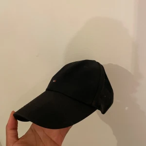 Tommy Hilfiger keps - Enkel svart keps från Tommy Hilfiger i bra skick. Den har en justerbar rem baktill för perfekt passform. Perfekt för vardagsbruk eller sportiga aktiviteter. Diskret logga på framsidan ger en stilren look.