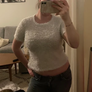 Vit fluffig kortärmad topp - Säljer en supermjuk och fluffig vit topp med korta ärmar. Perfekt för en mysig och stilren look. Toppen har en lätt glansig yta som ger den en unik touch.