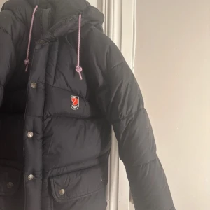 Svart fjällräven jacka  - Svart fjällräven jacka i storlek xxs, super varm o skön på vintern. jag har bytt original snörena men det går säkert att få tag i original om man vill.