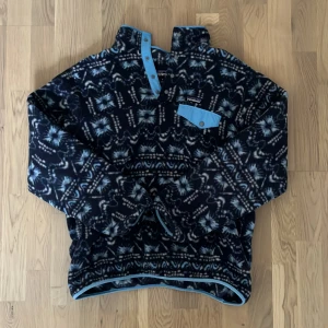 Mönstrad fleece från Patagonia - Säljer en snygg mönstrad fleece från Patagonia. Tröjan har en knappslå med ljusblå detaljer och en bröstficka med knapp. Perfekt för kyliga dar