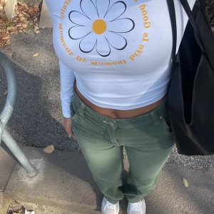 Vit långärmad croppad topp med blomtryck - Säljer en vit långärmad croppad topp från Bik Bok med ett stort blommönster och text i gult framtill. Perfekt för en avslappnad stil med en touch av färg. Passar bra till jeans eller kjol för en trendig look.