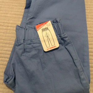 Blå byxor från LC Waikiki - Snygga blå paperbag-byxor från LC Waikiki för barn i åldern 11-12 år. Byxorna har en elastisk midja för extra komfort och stil. Perfekta för en avslappnad look med en modern touch. Aldrig använd. Prislapp på. 