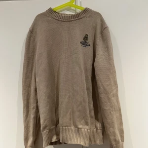 Beige stickad tröja från Morris - Säljer en stilren beige stickad tröja från Morris med broderad logga på bröstet. 