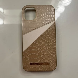 Mobilskal från Ideal of Sweden iphone 12 - Snyggt mobilskal från Ideal of Sweden med ormmönster och en vit diagonal detalj. Skalet har en elegant design och passar IPhone 12. Perfekt för att ge din mobil en stilren look. Skriv för fler bilder eller funderingar💕