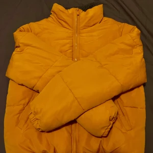 Gul pufferjacka från Vila - Säljer en snygg gul pufferjacka från Vila i storlek 36. Jackan har en dragkedja framtill och är fodrad med mjukt grått fleecefoder. Perfekt för kyliga dagar med sin varma och bekväma design. 🧥✨
