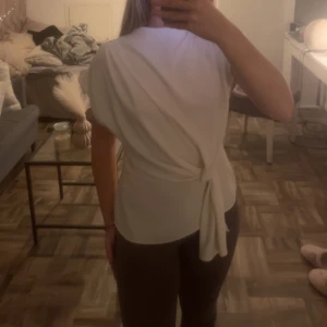 Vit omlottopp med knytband - Snygg vit omlottopp med knytband i midjan. Toppen har korta ärmar och en elegant design som passar perfekt för olika tillfällen. Den är tillverkad i ett mjukt och bekvämt material.