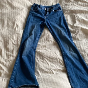 Blå bootcut jeans med stjärndetaljer - Snygga blå bootcut jeans med unika stjärndetaljer på bakfickorna. Jeansen är midwaist/low waist och stängs med dragkedja och dubbla knappar. Står storlek 152 men skulle själv säga att det är 146 då dom är rätt små i storlek 
