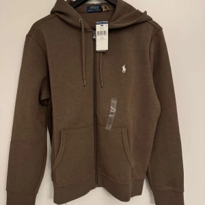 Brun hoodie från Ralph Lauren - Tjena, säljer en raulph lauren zip hoodie. Inköpt från raulph lauren butiken. Tröjan är helt sprillans ny med tags. Tar även emot bud. Ny pris cirka 2300 kr