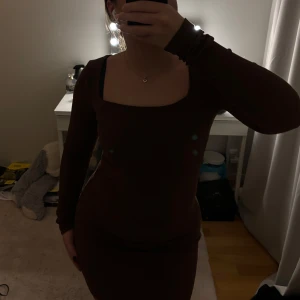 Brun ribbad klänning - Snygg brun klänning med ribbad struktur och långärmad design. Den har en tight passform som framhäver figuren och en stilren, enkel look. Perfekt för en chic och avslappnad stil.