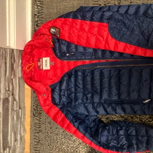 Röd och marinblå dunjacka från Parajumpers - Säljer en snygg röd och marinblå dunjacka från Parajumpers, modell Sheen. Jackan har en cool patch på ärmen och dragkedja framtill. Perfekt för kyliga dagar med sin quiltade design.