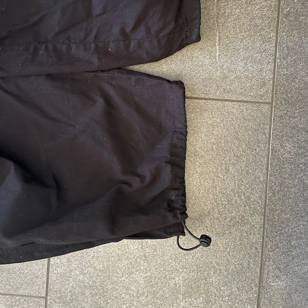 Svarta byxor från RAP med elastisk midja och dragsko vid bensluten. Perfekta för utomhusaktiviteter med en bekväm passform. Tillverkade i ett slitstarkt material som passar bra för olika väderförhållanden. (Prislapp kvar, första bilden lånad men exakt samma byxa). Farkut & Housut.