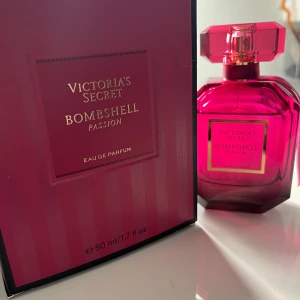 Victoria's Secret Bombshell Passion Eau de Parfum - Säljer en lyxig och feminin parfym från Victoria's Secret, Bombshell Passion. Flaskan är i en djup rosa färg med en elegant design. Perfekt för den som vill ha en doft som utstrålar självsäkerhet och stil.