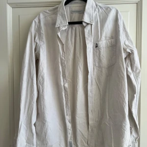 Vit skjorta från Peak Performance - Säljer en stilren vit skjorta från Peak Performance i storlek M. Skjortan har en klassisk krage och en bröstficka med en liten broderad detalj. Den är långärmad och har knappar framtill. Perfekt för en avslappnad men ändå snygg look.