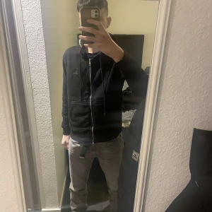 Svart jacka från Burberry - Säljer en stilren svart jacka från Burberry med dragkedja och långa ärmar. Jackan har en klassisk design med en diskret logga på bröstet. Perfekt för en elegant look.